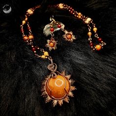 a necklace with an orange stone surrounded by beads and other jewelry items on a black fur surface