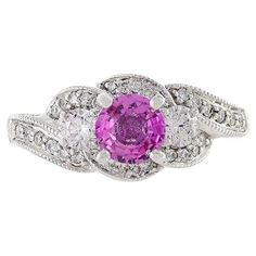 This 14KT white gold ring is a stunning and elegant piece of jewelry, featuring a genuine round-cut Ceylon pink sapphire with a weight of 1.02 carats at its center. The pink sapphire is beautifully surrounded by a swirling design of round-cut diamonds, with a total weight of 1.00 carats. These diamonds exhibit G-H color and SI1-SI2 clarity, ensuring a brilliant and high-quality sparkle. This ring is a luxurious and sophisticated accessory, perfect for adding a pop of color and a touch of elegance to your hand, with the captivating pink sapphire as the focal point. Size 7.5 US. Weight 5.9 gm. Swirl Diamond Ring, Swirl Ring, White Gold Ring, Gorgeous Jewelry, Sapphire Diamond, Round Cut Diamond, Pink Sapphire, White Gold Rings, Earings Piercings