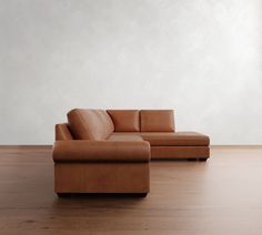 a brown leather couch sitting on top of a wooden floor next to a white wall