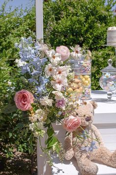 a teddy bear sitting next to a bouquet of flowers on a white porch chair outside