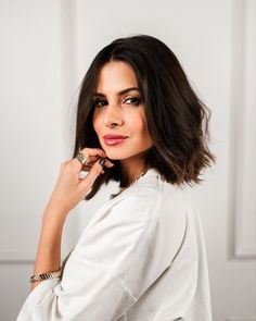 a woman posing with her hand on her chin and looking at the camera while wearing a white shirt