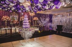 purple and white balloons are hanging from the ceiling above a table with a cake on it