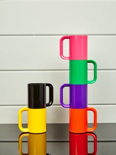 three different colored coffee mugs sitting next to each other on a table with white boards in the background