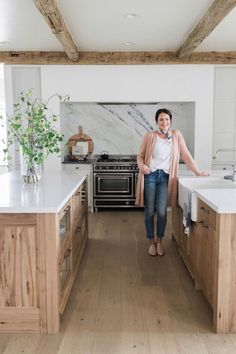 a woman standing in the middle of a kitchen with an oven, sink and counter top