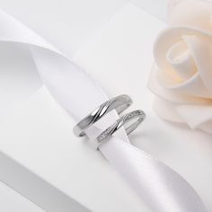 two wedding rings sitting on top of a white cloth next to a rose and ribbon