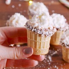 a hand holding an ice cream cone with chocolate sprinkles and white frosting