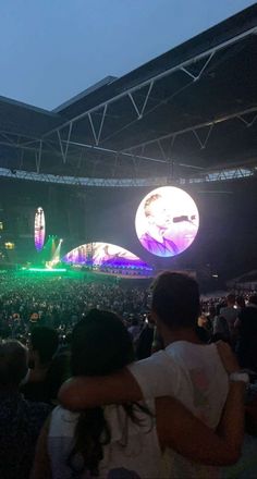 the crowd is watching an outdoor concert at night with lights on and large screens in the background