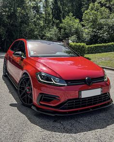 a red volkswagen golf gtr is parked on the side of the road in front of some trees