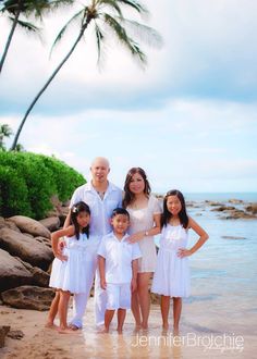 a family standing on the beach in front of some water and palm trees with their arms around each other