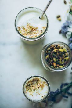 two glasses filled with yogurt and granola on a white table next to flowers