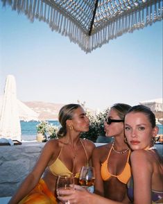 two beautiful women sitting next to each other holding wine glasses in front of an umbrella