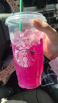 a person holding up a pink starbucks cup with ice and sprinkles on it