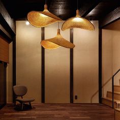 three lamps hanging from the ceiling in a room with wooden floors and stairs, along with a chair