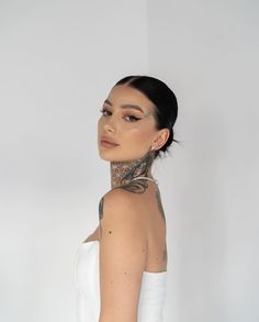 a woman with tattoos on her neck wearing a white dress and looking off to the side