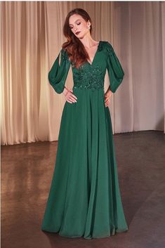 a woman in a long green dress standing next to a white curtain with her hands on her hips