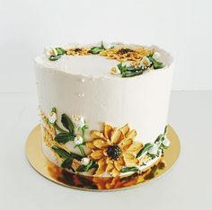 a white cake with yellow flowers and green leaves on the top is sitting on a gold plate