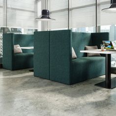 an office cubicle with two green booths and a white table in the middle, surrounded by windows