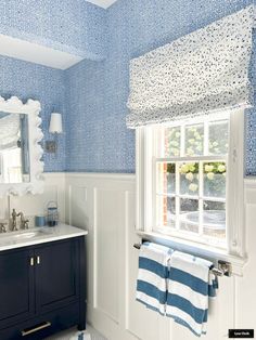 a bathroom with blue and white wallpaper, two towels hanging on the window sill