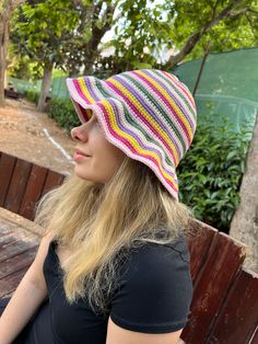 a woman sitting on a wooden bench wearing a colorful crochet knitted hat