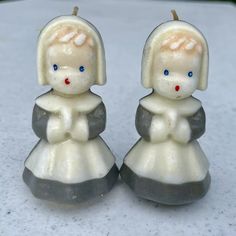 two small candles sitting next to each other on top of a white tablecloth covered surface