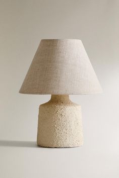 a white lamp with a beige shade on it's base and a light bulb in the middle