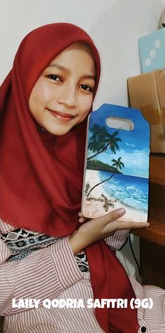 a woman in a red hijab holding up a cell phone case with an image of a beach on it