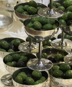 several silver bowls filled with green olives on a table