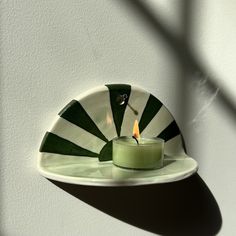 a green candle sitting on top of a white plate next to a shadow of a wall