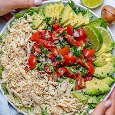 two hands holding a salad with chicken, avocado and tomatoes on it in a white bowl