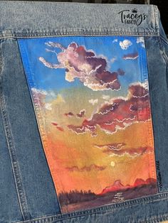 the back of a jean jacket with an image of clouds painted on it's side