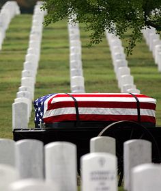 an american flag covered casket sitting in the middle of a cemetery with white headstones