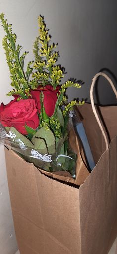 a brown paper bag with red roses and greenery in it sitting on the floor