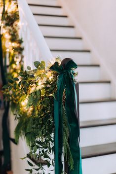 a green ribbon tied to the banister with greenery and lights on it's side