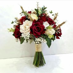 a bouquet of red and white flowers in a vase with greenery on the side