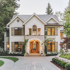 a large white house with lots of windows and plants on the front door, surrounded by greenery