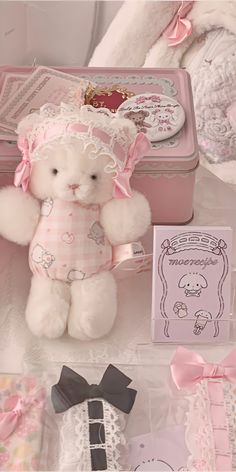 a white teddy bear sitting on top of a table next to a pink box and other items