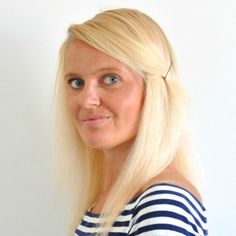 a woman with long blonde hair and blue eyes posing for a photo in front of a white wall