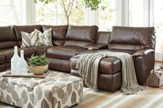 a living room with brown leather furniture and pillows on the couch, coffee table and footstool