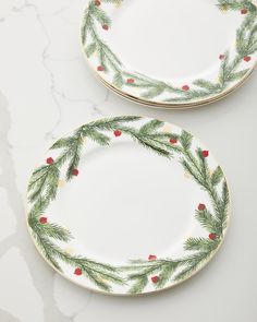 two plates decorated with pine branches and red berries on white marble counter top, one has gold trim