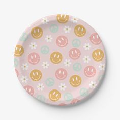 a pink paper plate with smiley faces and daisies on the rim, against a white background