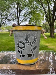 a flower pot sitting on top of a glass table in front of some grass and trees