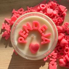 a cup filled with lots of pink letters on top of a wooden table next to small hearts