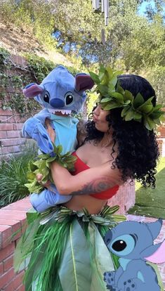 a woman holding a stuffed animal next to a brick wall with plants on her head