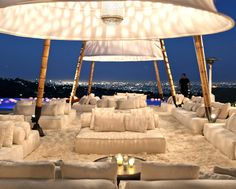 an outdoor seating area with white couches and pillows on the ground at night time