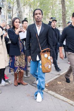 a man is walking down the street carrying a brown purse and people are standing around him