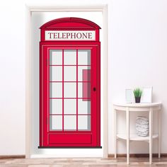 a red phone booth on the side of a wall next to a table and chair