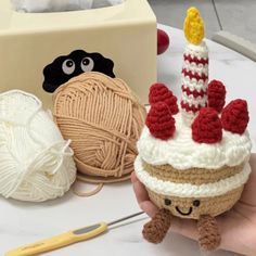 a hand holding a small cupcake with a candle on it next to yarn and crochet