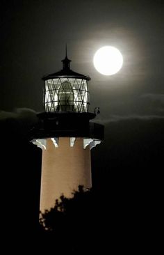 the moon is setting behind a light house