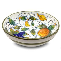 a bowl with fruit and leaves painted on the side, sitting in front of a white background