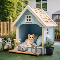 a dog is sitting in a small blue house with flowers and potted plants on the lawn